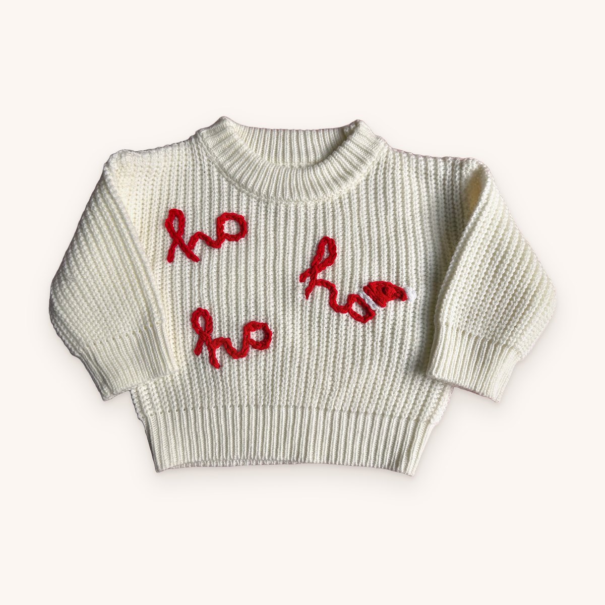 Cream chunky knit Christmas jumper with ho ho ho hand-embroidered in red chain-stitch script, the last o wearing a little red and white Santa hat