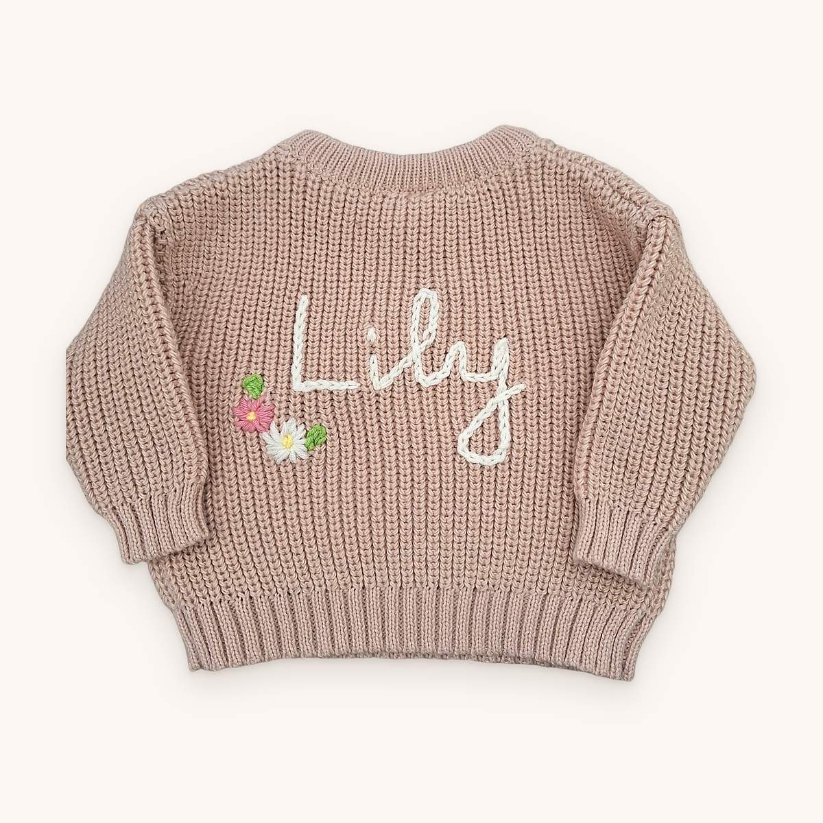 Dusty pink chunky knit baby jumper with the name Lily hand-embroidered in cream chain-stitch script, with a small cluster of embroidered pink and white flowers and green leaves